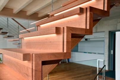 Das Bild zeigt eine elegante beleuchtete Holmentreppe aus Holz mit Glasgeländer