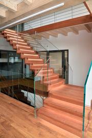 Das Bild zeigt eine elegante beleuchtete Holmentreppe aus Holz mit Glasgeländer